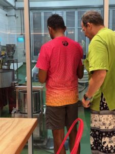 Two participants are observing the chocolate-making process through a glass window at Siamaya Chocolate Factory, watching as cocoa beans are processed.