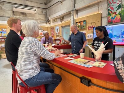 A group of people listening attentively to a chocolate-making demonstration, with various ingredients and chocolate products displayed.