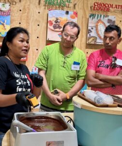 A participant is focused on molding their chocolate bar with creative toppings, following the guidance of the instructor at Siamaya Chocolate Factory.