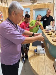 A participant is adding chocolate to molds at a work station during the interactive chocolate-making session, with others observing.