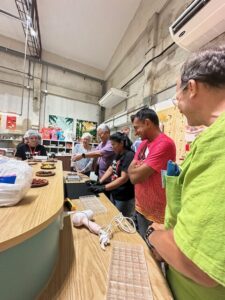 Several participants are gathered around the counter, involved in the chocolate-making process and working on their own chocolate bars, with an instructor guiding them.