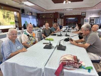 Participants of the Chiang Rai excursion gather in a meeting room, sitting at a table set up for a discussion. The image shows a group of people, including a few wearing name tags, engaged in the learning process as they prepare for the next part of their journey, reflecting the informative and interactive nature of the trip.
