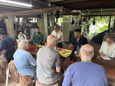 Participants in the Chiang Rai excursion engage in a lively discussion with local community members in a rustic setting. The image captures the exchange of ideas, with both visitors and locals actively participating in the conversation, emphasizing the collaborative learning experience in this culturally rich environment