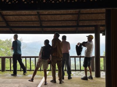 Participants in the Chiang Rai excursion pause to take in the breathtaking view of the surrounding mountains. The image captures them from behind as they admire the lush landscape, reflecting the tranquility and natural beauty that defines this upland region.