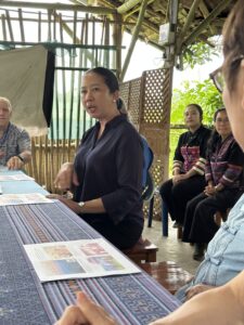 A local leader from the Chiang Rai community speaks to the group, sharing valuable insights on the region's culture and development. The image captures the leader in the midst of a discussion with participants, emphasizing the importance of direct engagement and learning during the excursion.