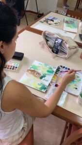 Student practices wet-on-wet technique while painting a house and trees.