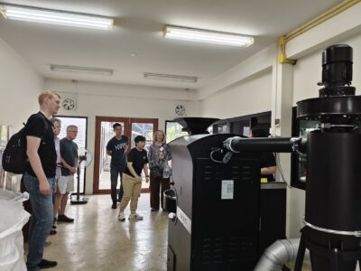 The group visits the roastery, observing roasting equipment as they learn how beans transform from green to aromatic coffee