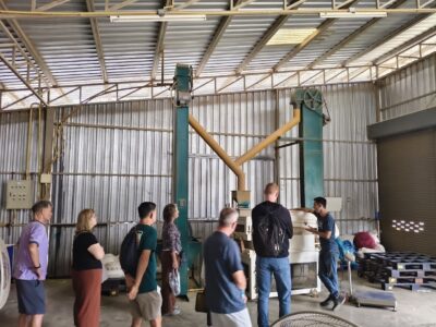 Inside the warehouse, participants tour the hulling and grading machinery used to prepare beans to international standards.