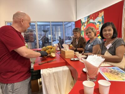 A workshop instructor presents fresh cocoa pods to Lifelong Learning participants seated at a tasting counter.