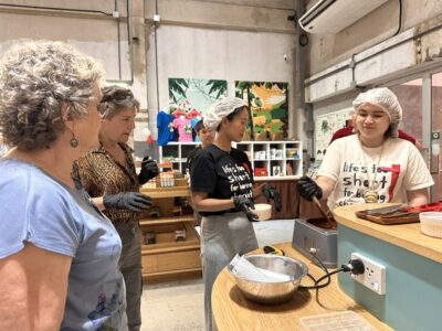 Participants gather around a counter to watch a Siamaya Chocolate staff member stir a batch of melted chocolate.