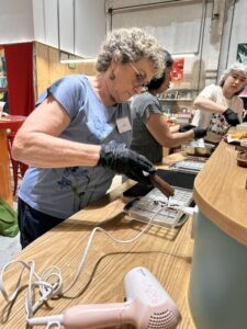 A participant wearing black gloves pipes chocolate into a mold next to a hair dryer used for temperature control.