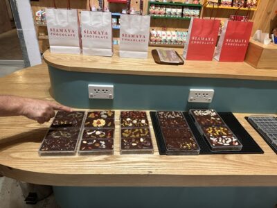 A row of custom-made chocolate bars topped with assorted fruits and nuts sits on the counter in clear molds.